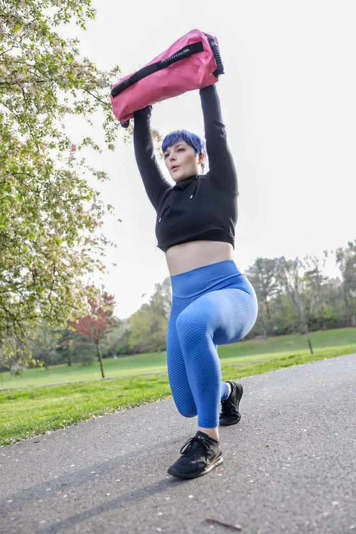 Rachel training outdoors with a sandbag overhead